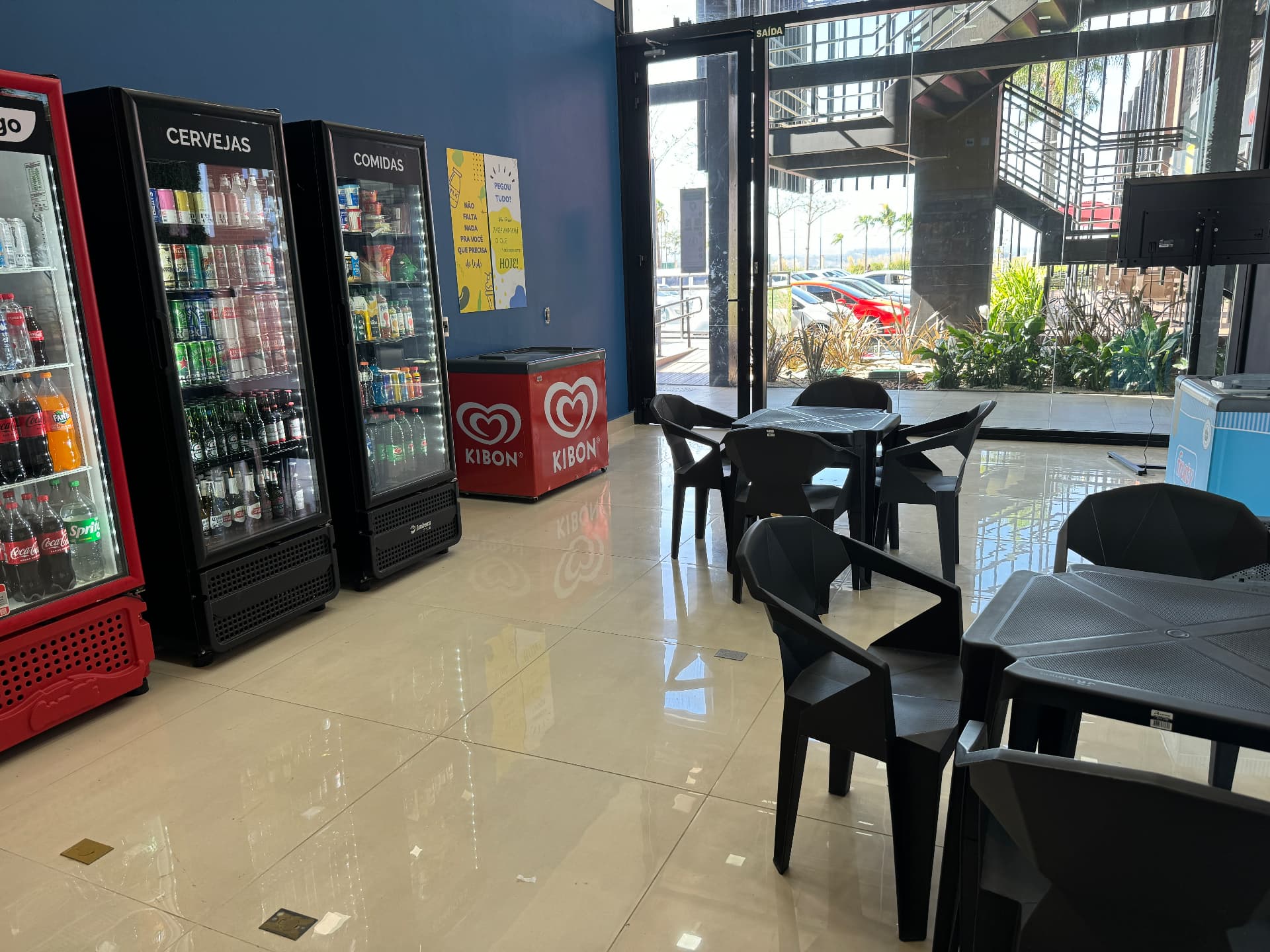 Área de convivência da loja Omnimart com geladeiras de bebidas e mesas